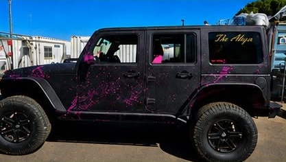 Black Jeep with pink paint graphics in an industrial yard